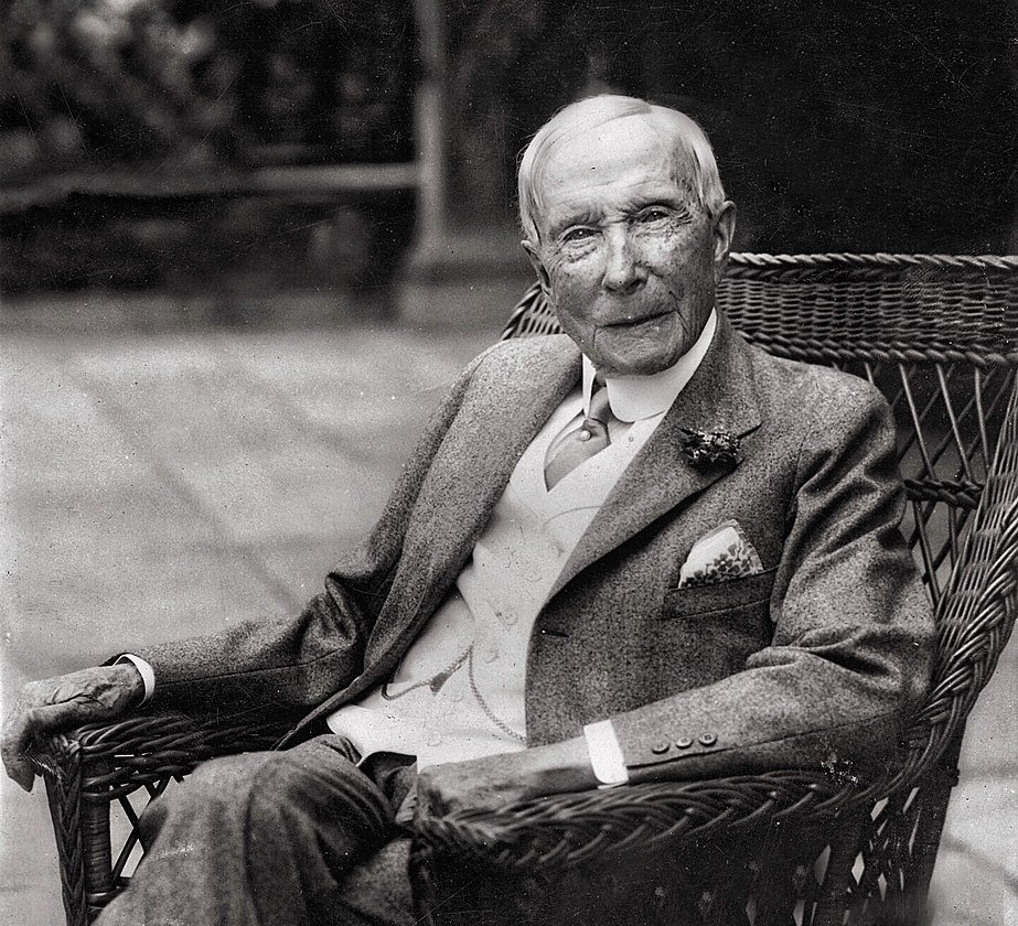 Grayscale Portrait Photo of old John D. Rockefeller sitting on a chair
