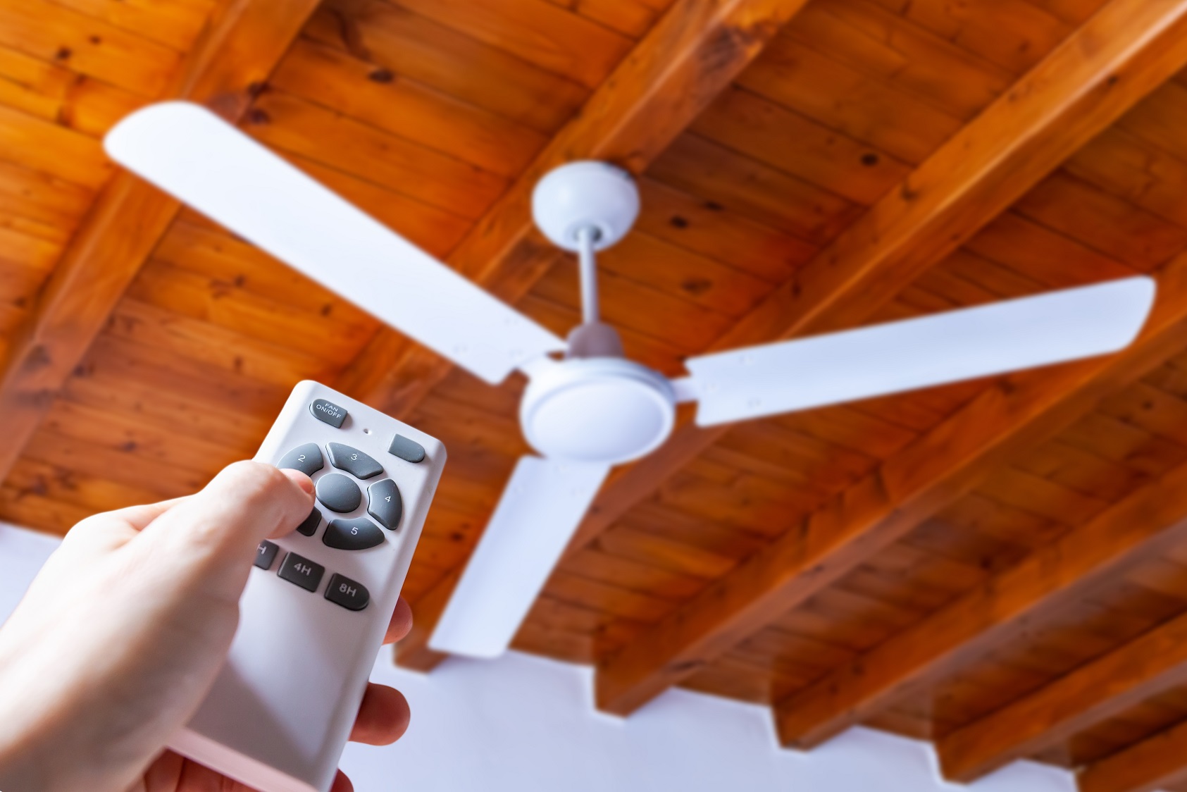 A man uses a remote control to turn on a white ceiling fan.
