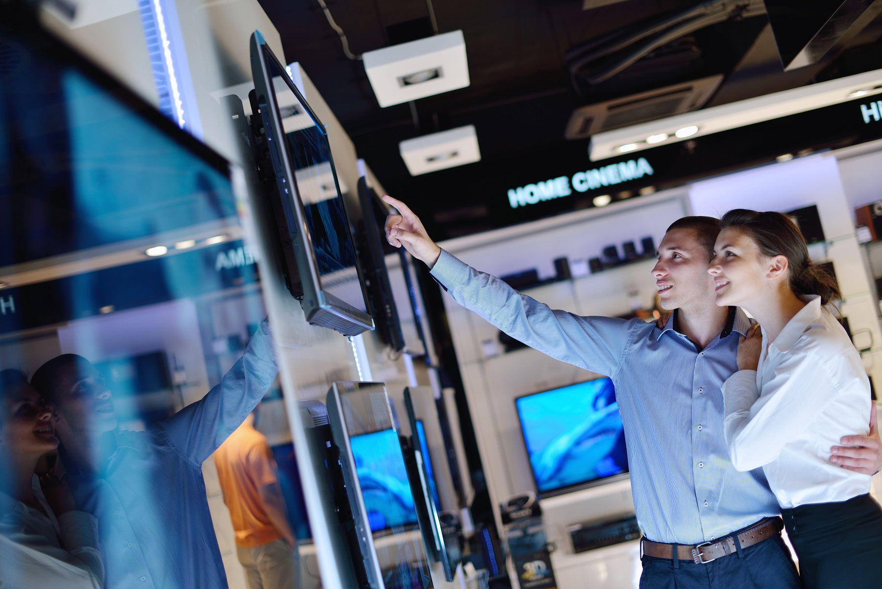Young couple in consumer electronics store looking at television and to buy.