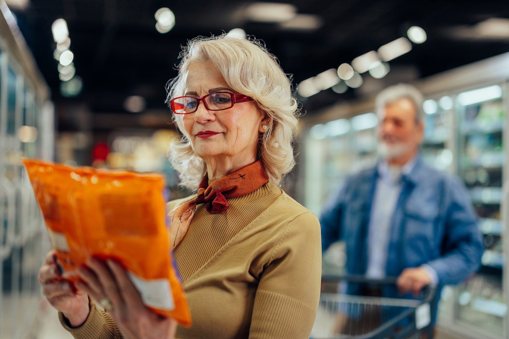 Smiling woman shopping in supermarket and reading product information.