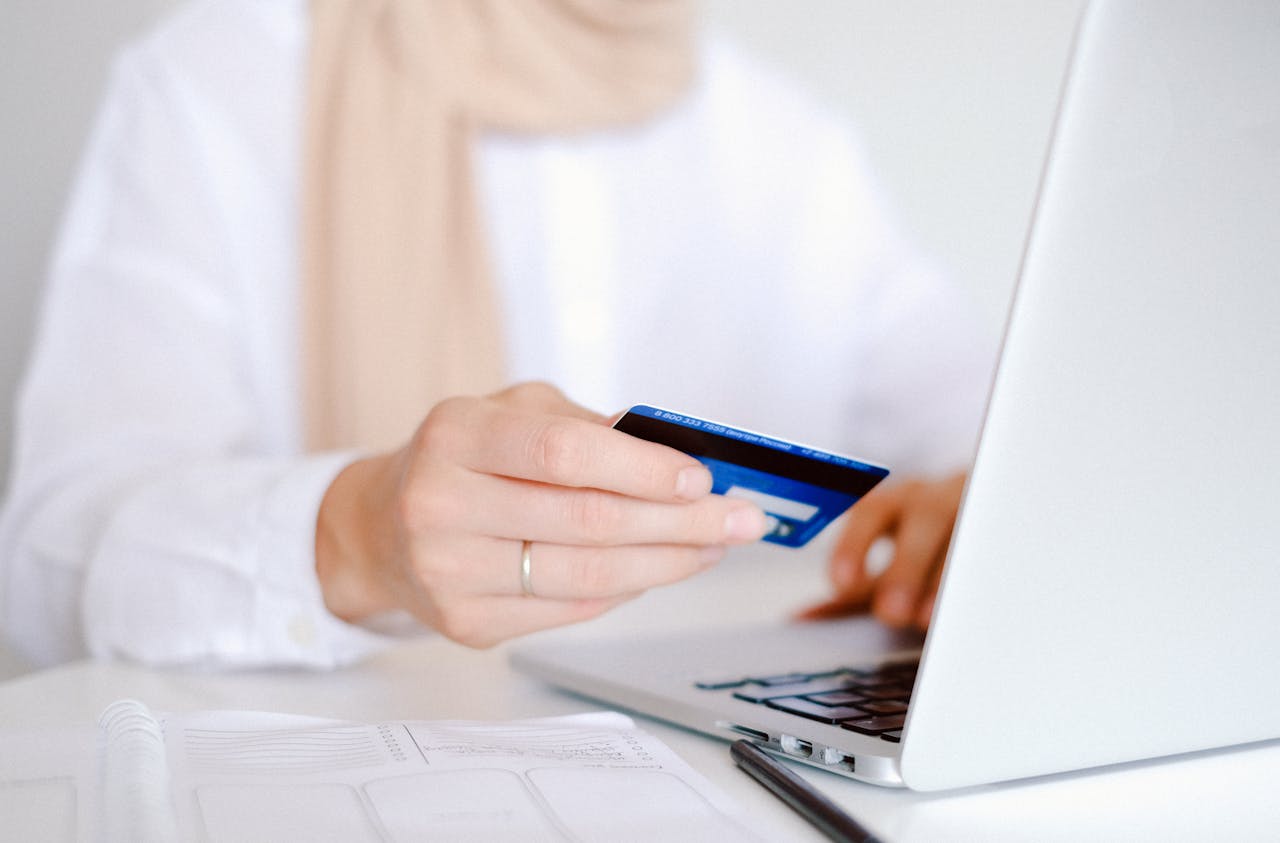 Person in White Long Sleeve Shirt Holding Credit Card in front of a laptop