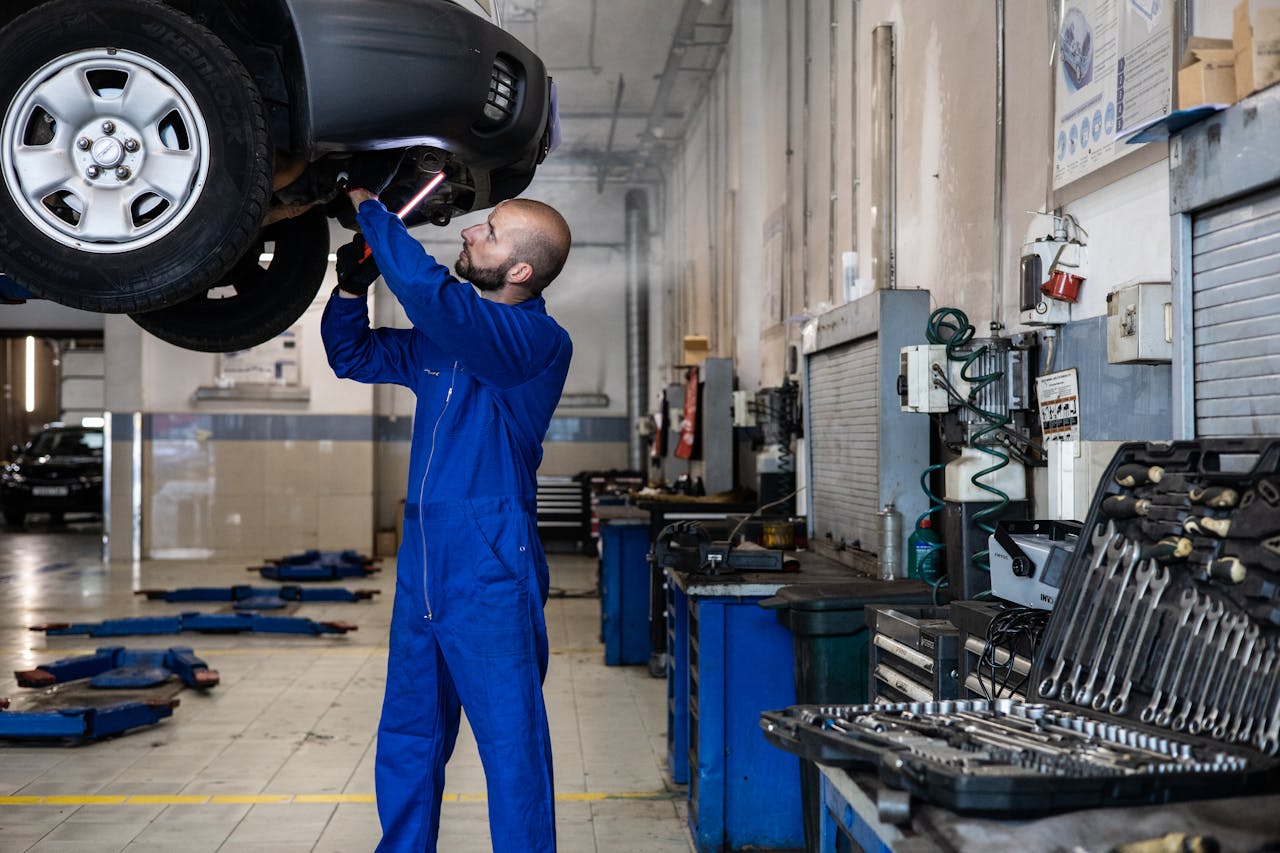 A Man in Blue Suit Checking a Car in a vehicle repair shop