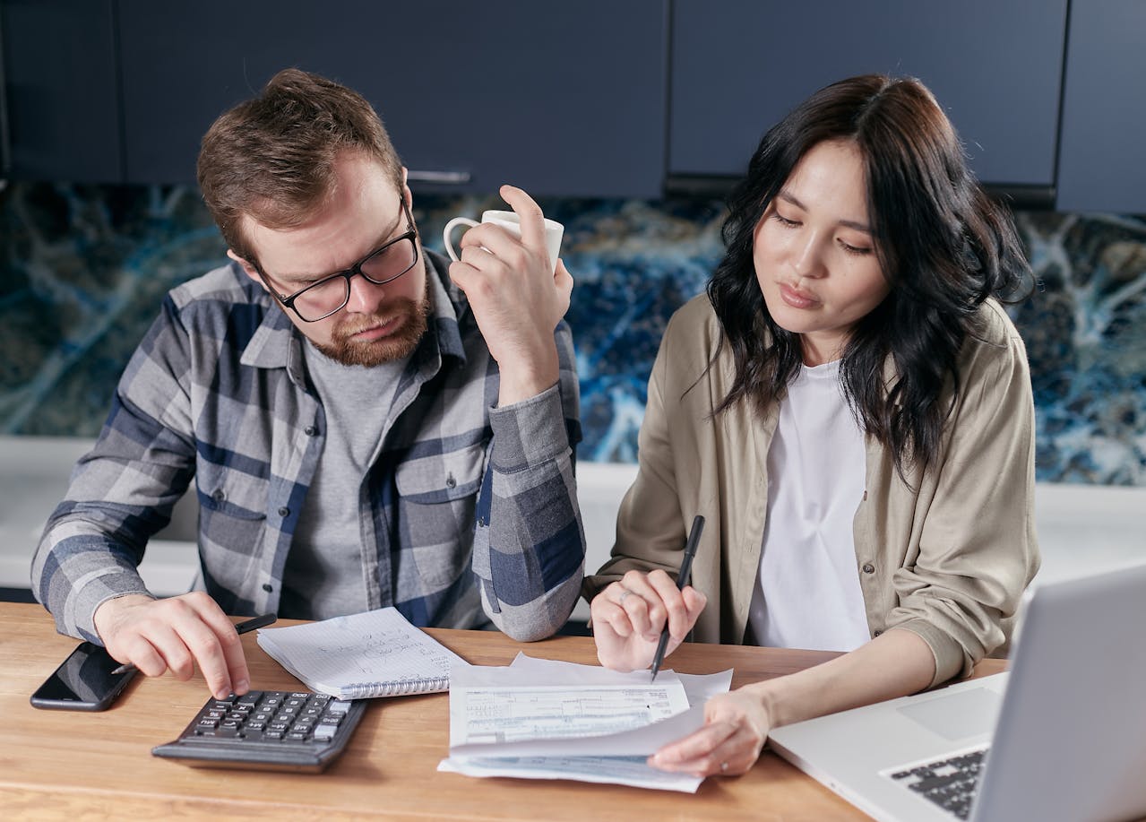 Couple sitting on a wooden desk Looking at their Bills, lap top in front