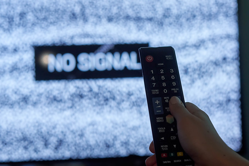 A hand holding tv remote over the TV display with 'No signal' sign