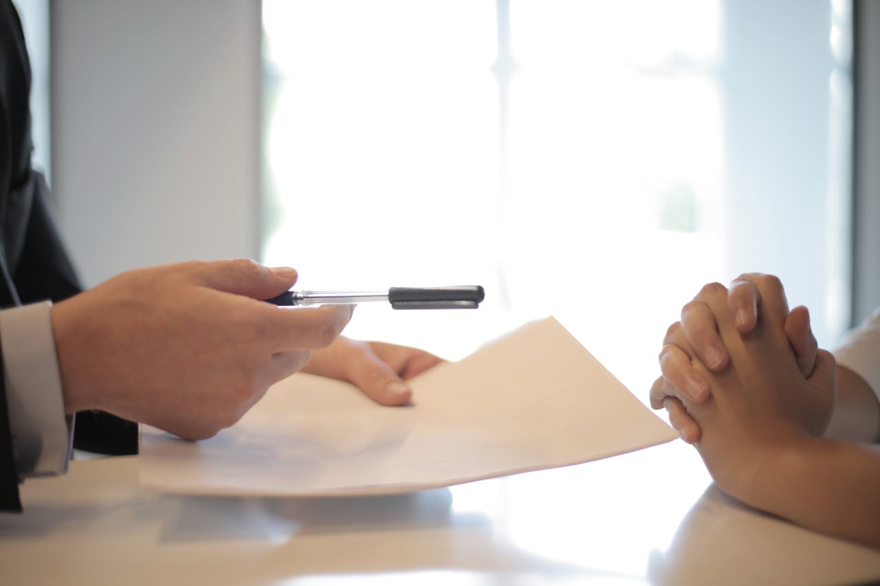 Businessman giving contract to woman to sign sitting on a desk