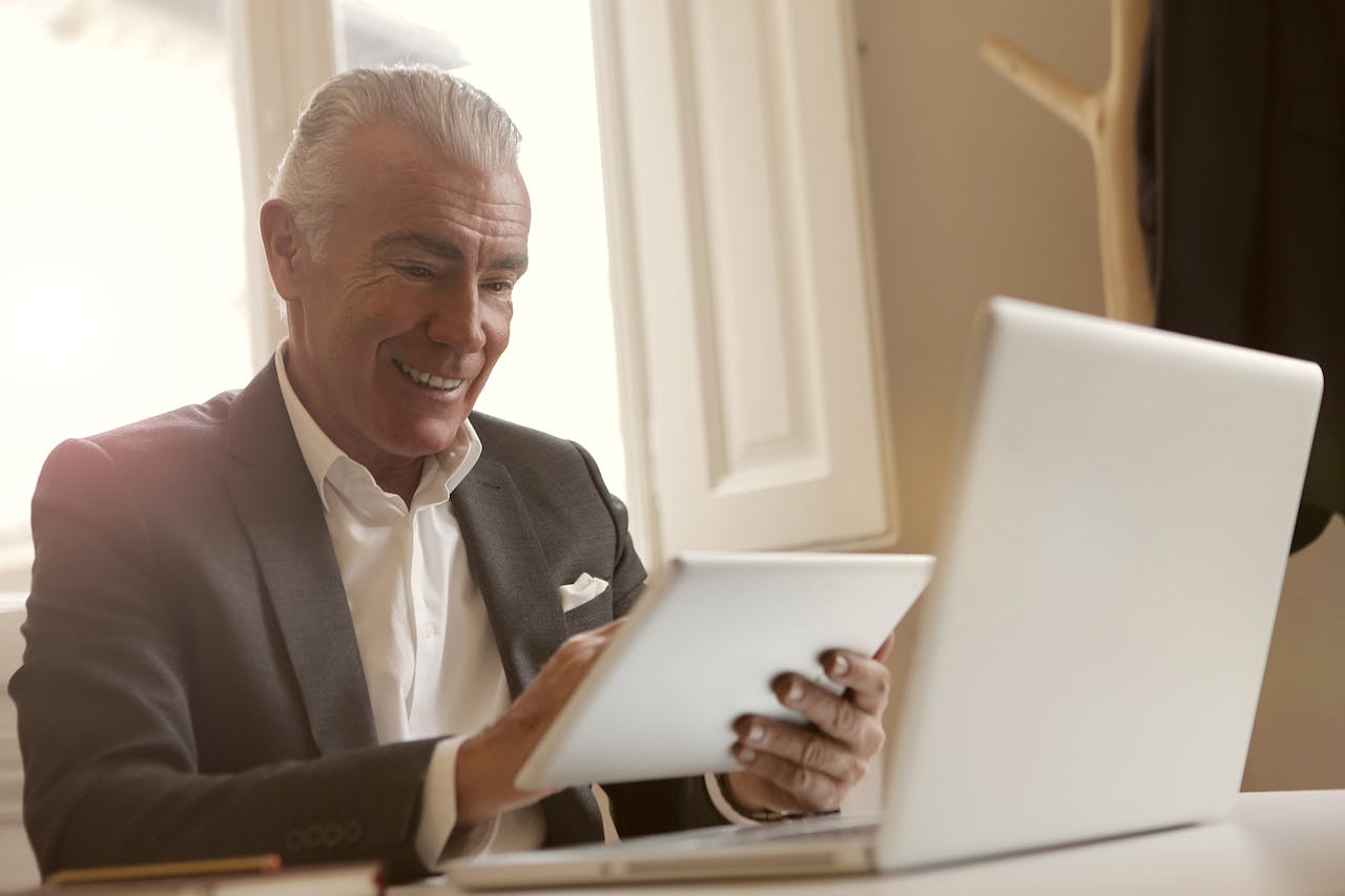 Elderly man in dark suite holding a tablet sitting on office desk
