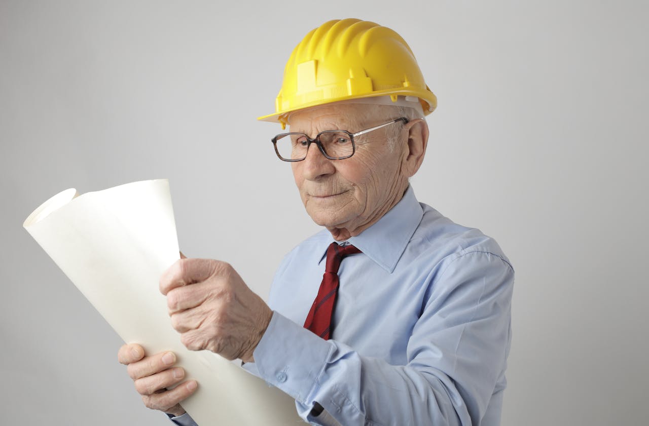 Senior male engineer reading blueprint wearing a protective yellow helmet
