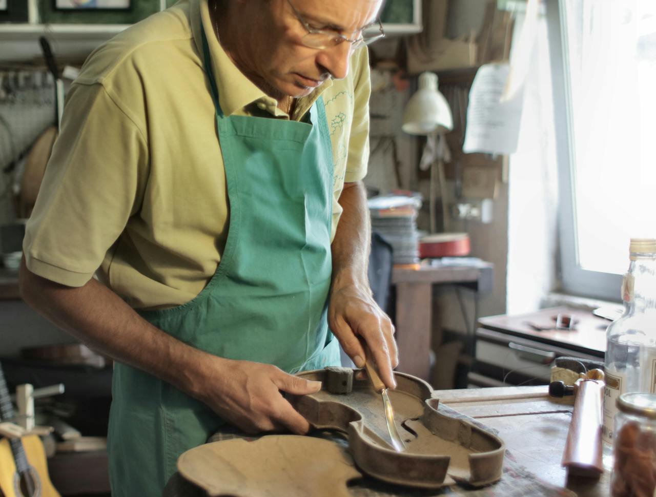 Male artisan cutting violin from tree in workplace