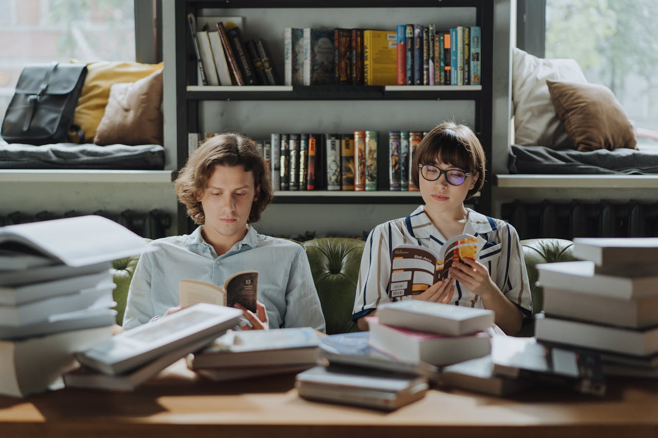 Photo of a young man and woman sitting next to each other reading a books