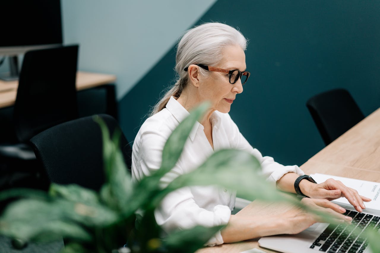 Older woman sitting on a desk using laptop inside an office