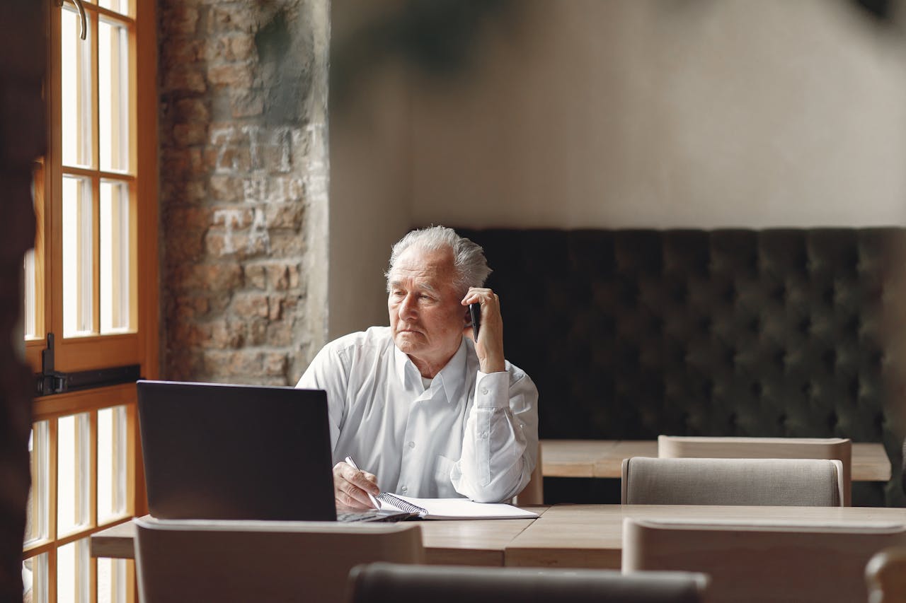 Pensive stylish elderly man speaking on smartphone in creative office