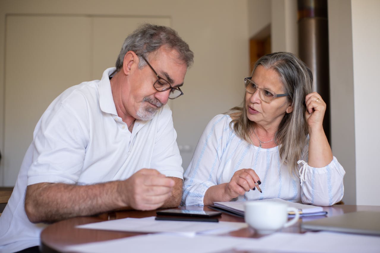 Elderly couple sitting on a wooden table completing documents and talking to each other