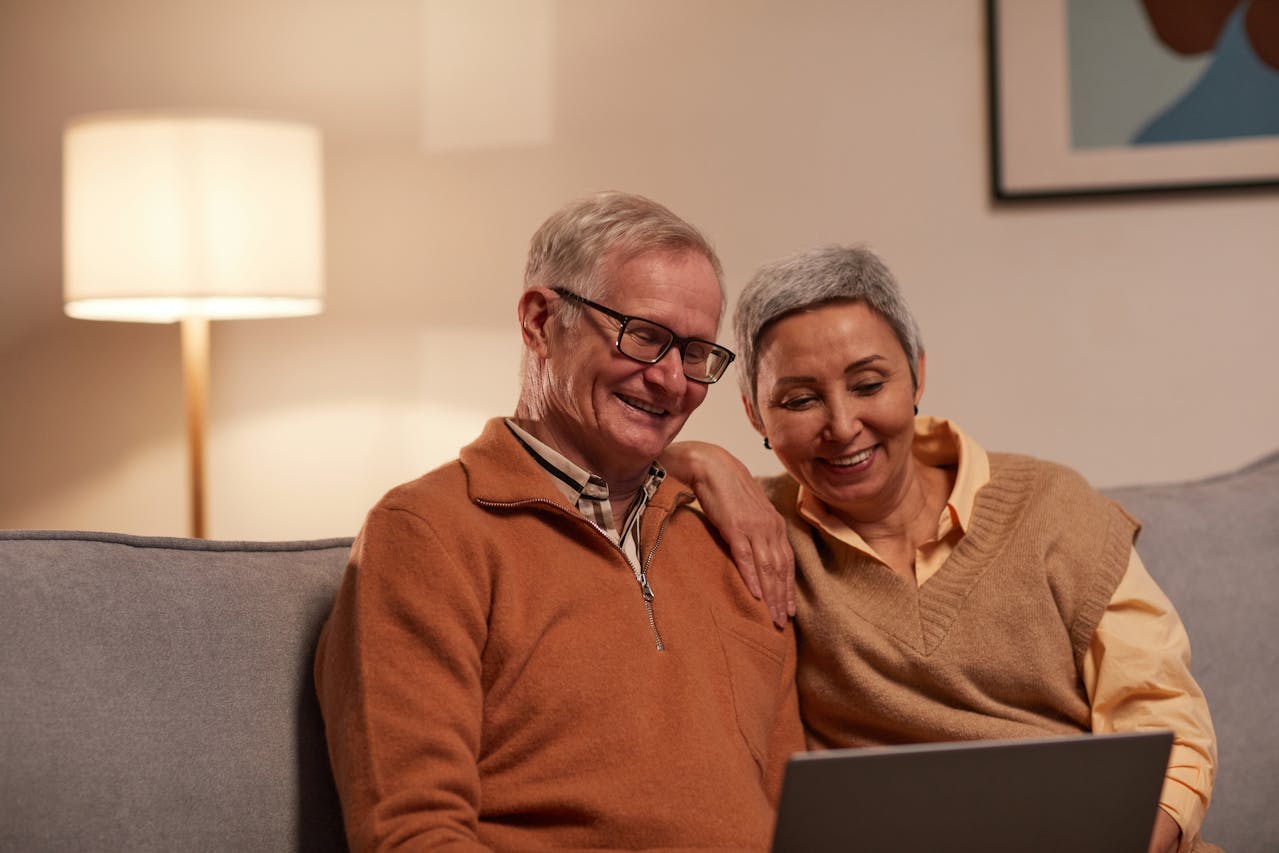 Man and woman sitting on sofa and smiling while looking at a laptop