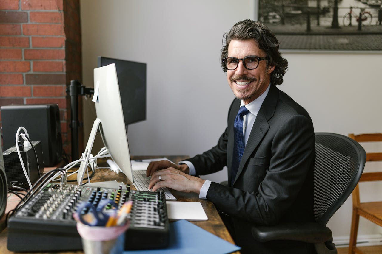 Photo of man in black suit-smiling while typing on computer keyboard