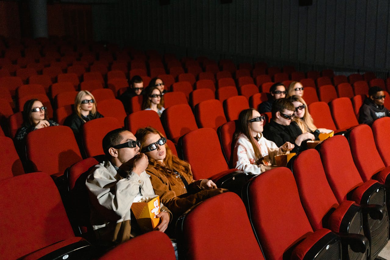 People sitting on red chairs in a Movie Theater eating popcorns