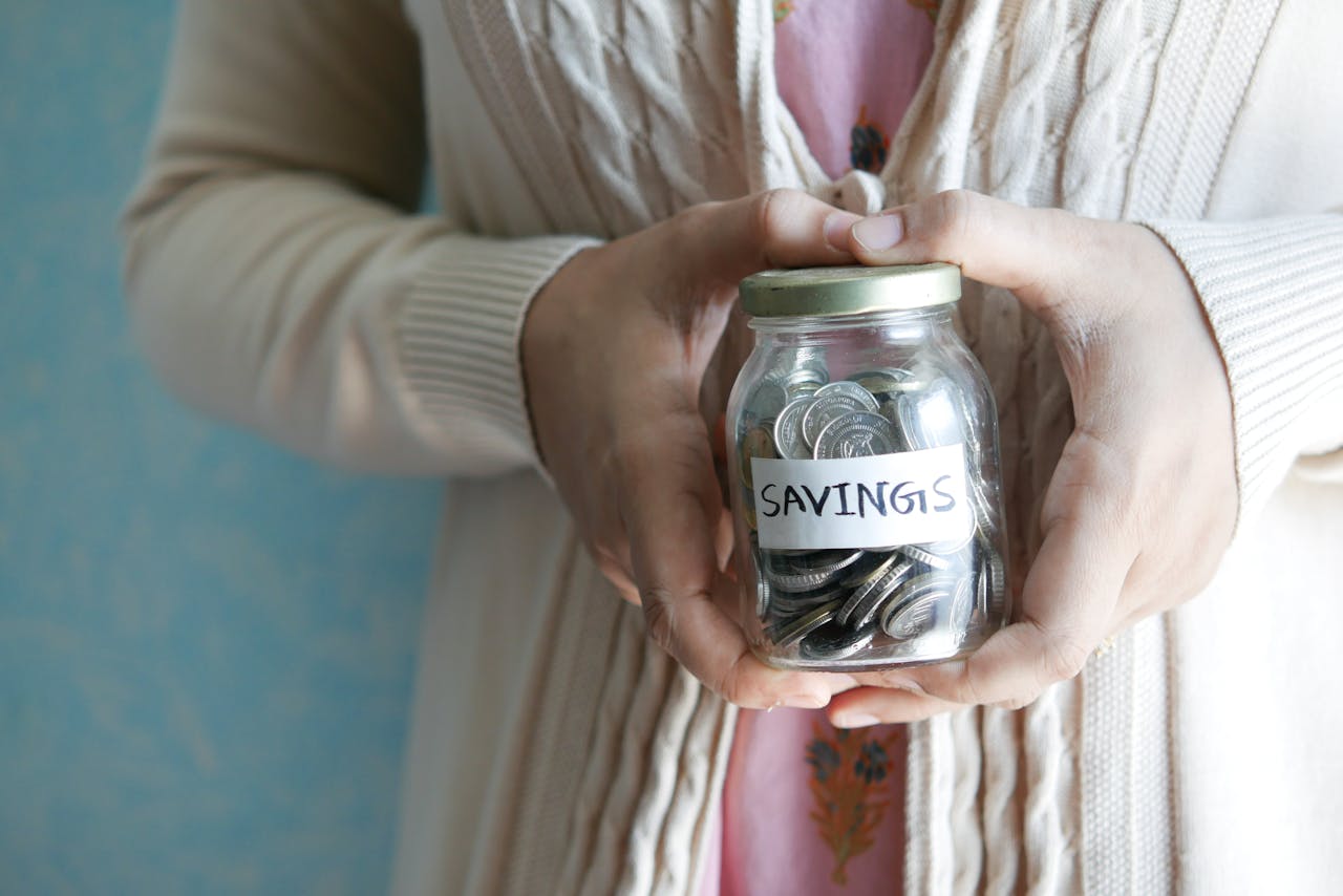 Person holding a jar with savings label filled with coins
