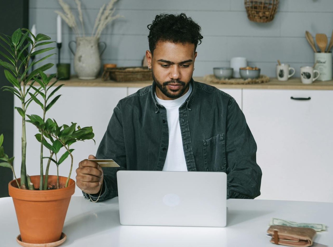 Man Holding a Card While Looking at the Screen of a Laptop