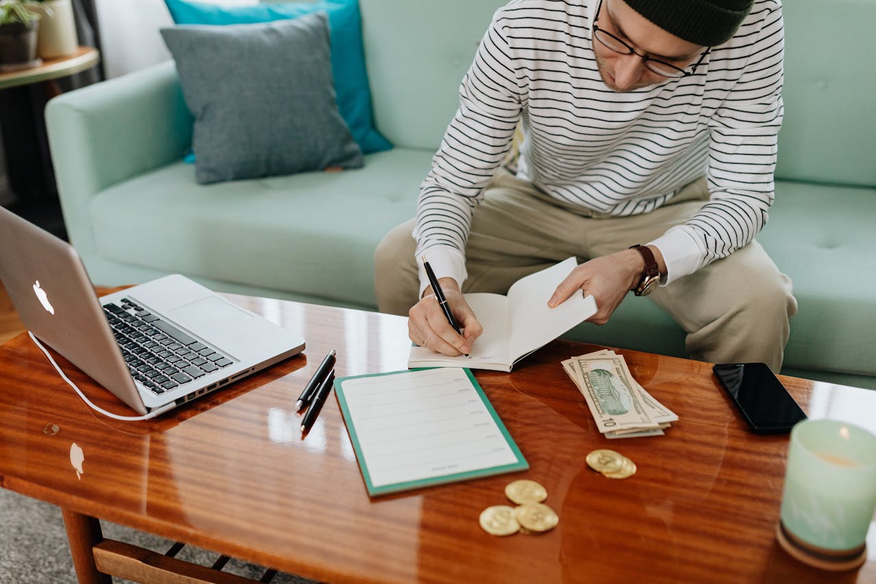 Man Writing on a Notebook next to pile of money