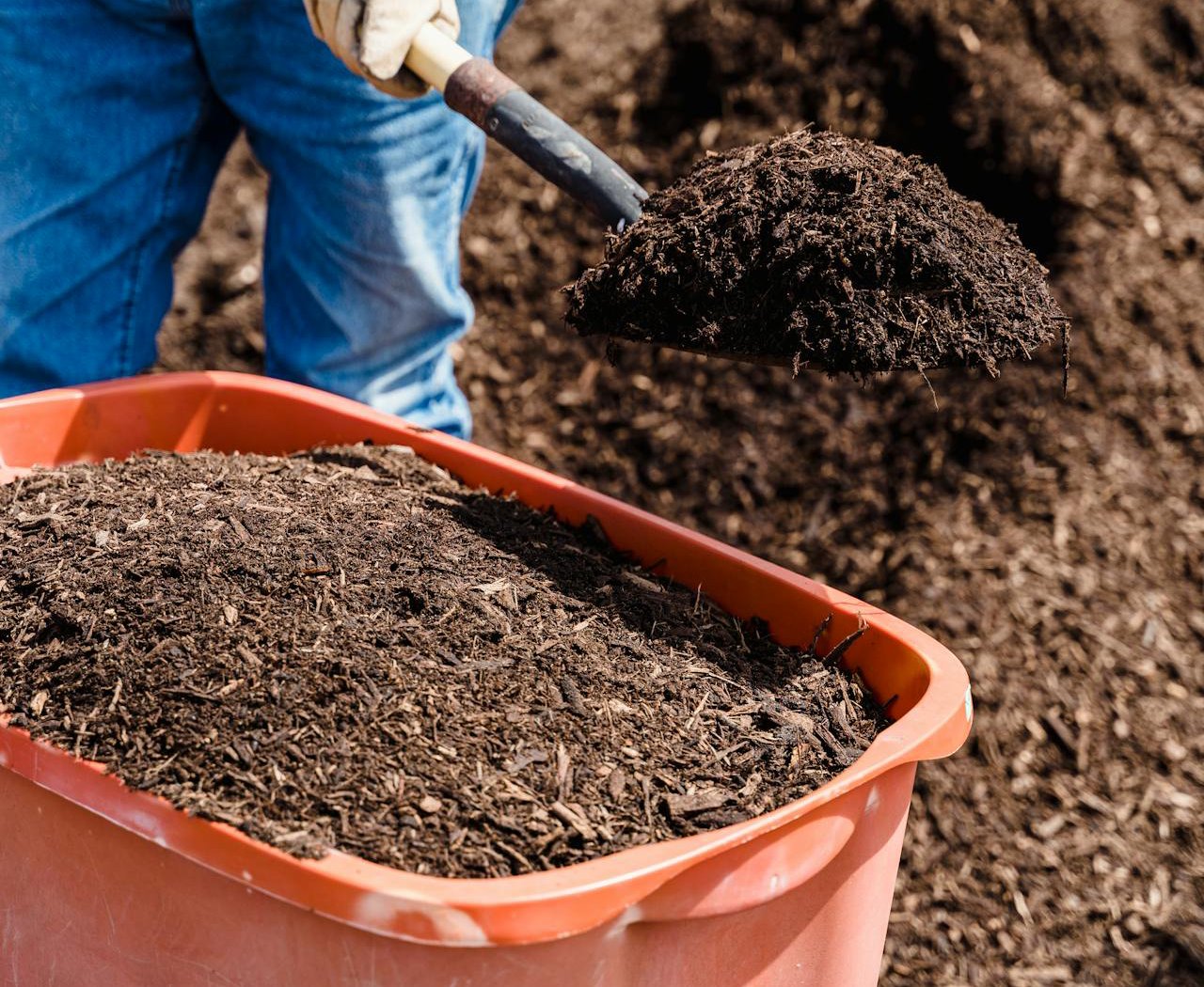 Close Up Photo of of a Person filling Brown Soil in Orange Plastic Bucket