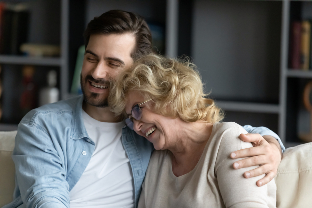 Close up of grown up child son hugs elderly mother