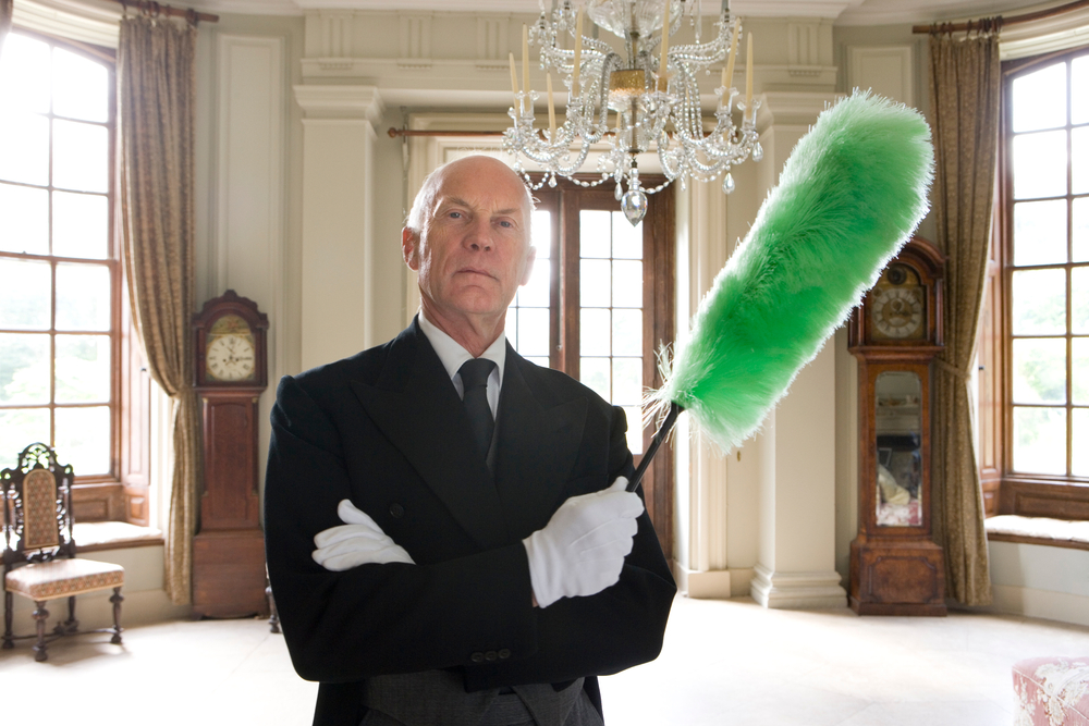 Horizontal shot of a butler standing with arms crossed and holding a duster