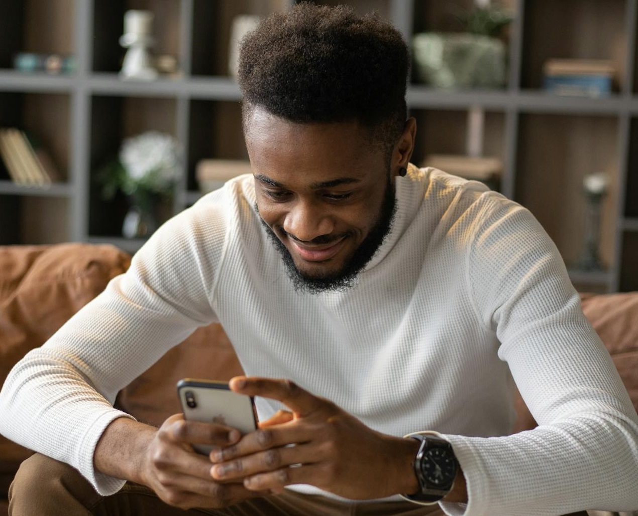 Happy man using smartphone while sitting on sofa.