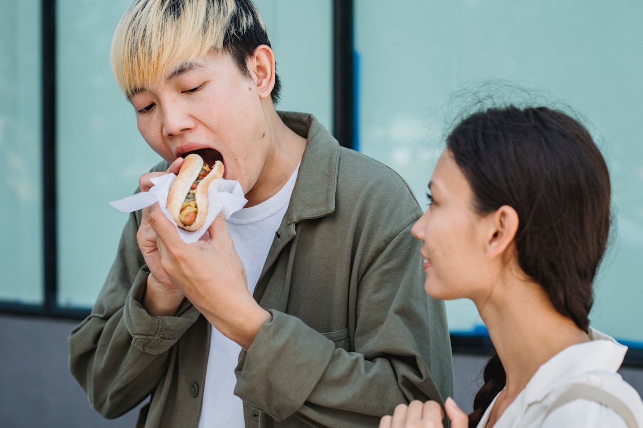 Asian man eating hot dog near young girlfriend