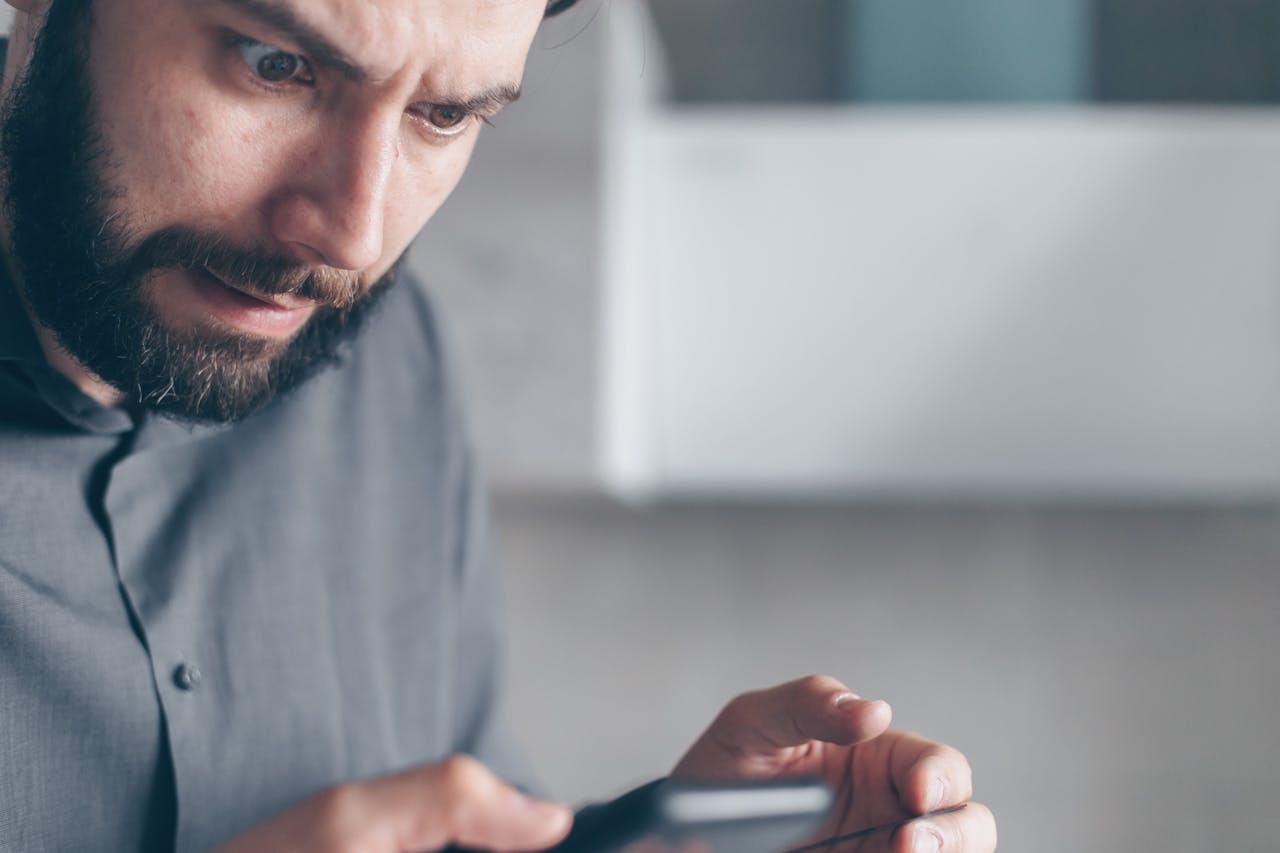 Shocked Man in Gray Shirt Looking at a Smartphone