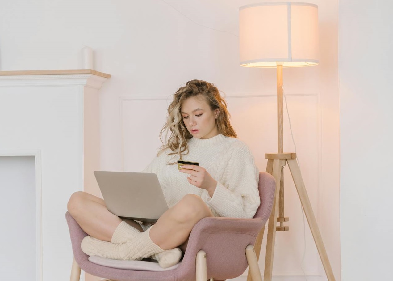 A Woman Sitting on a Chair Holding a Card while Browsing the Laptop