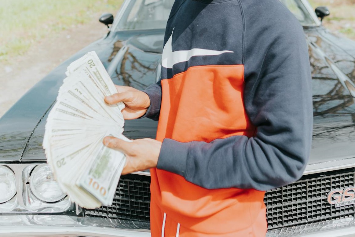 Young Man is Holding Money in front of a car.