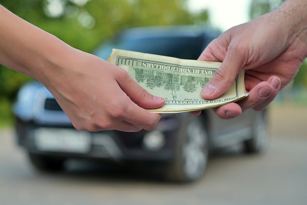 Woman gives cash to a man when buying a car. The car is out of focus
