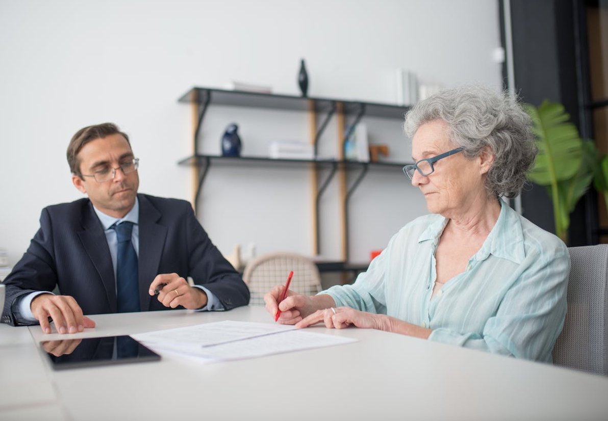 Elderly Woman in Blue Shirt Signing Documents