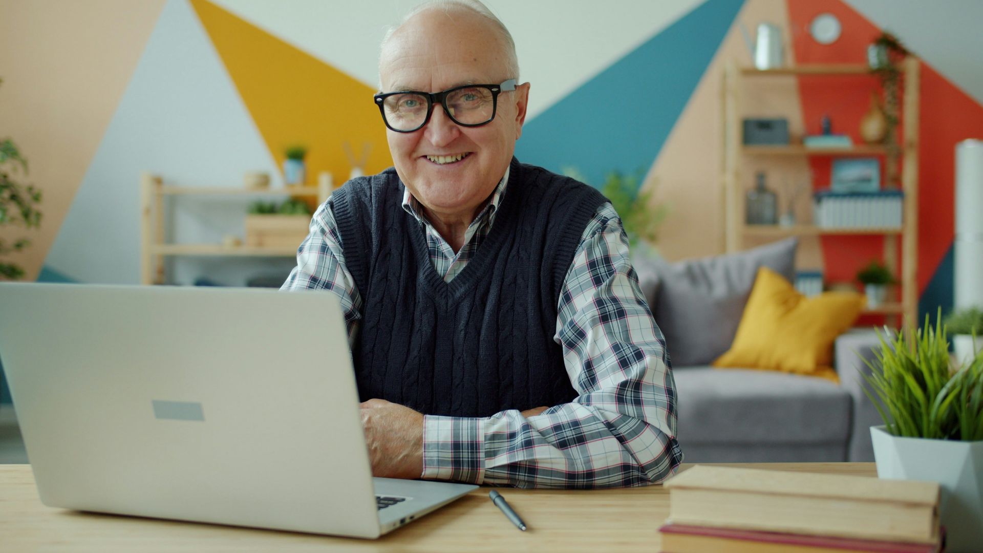 Smiling elderly man with glasses at laptop computer.