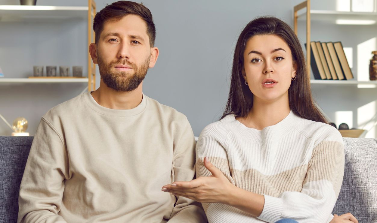 man and a woman sitting on a gray couch in a modern, well-lit living room