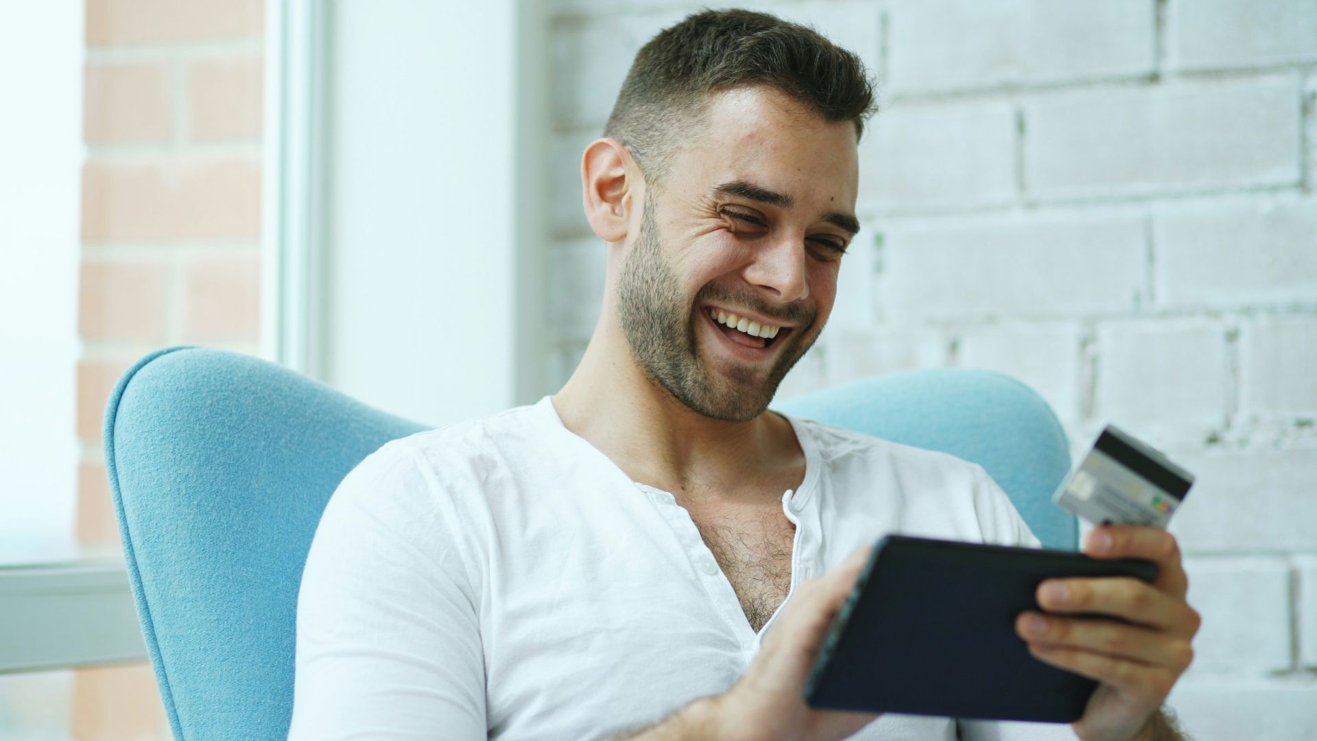 Man laughing while holding credit card and tablet.