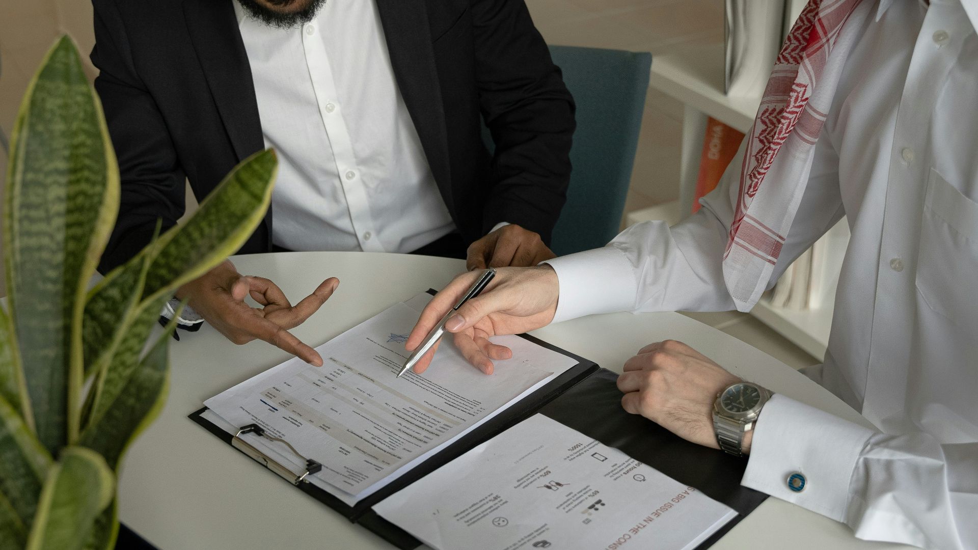 two men sitting at a table with papers and a pen