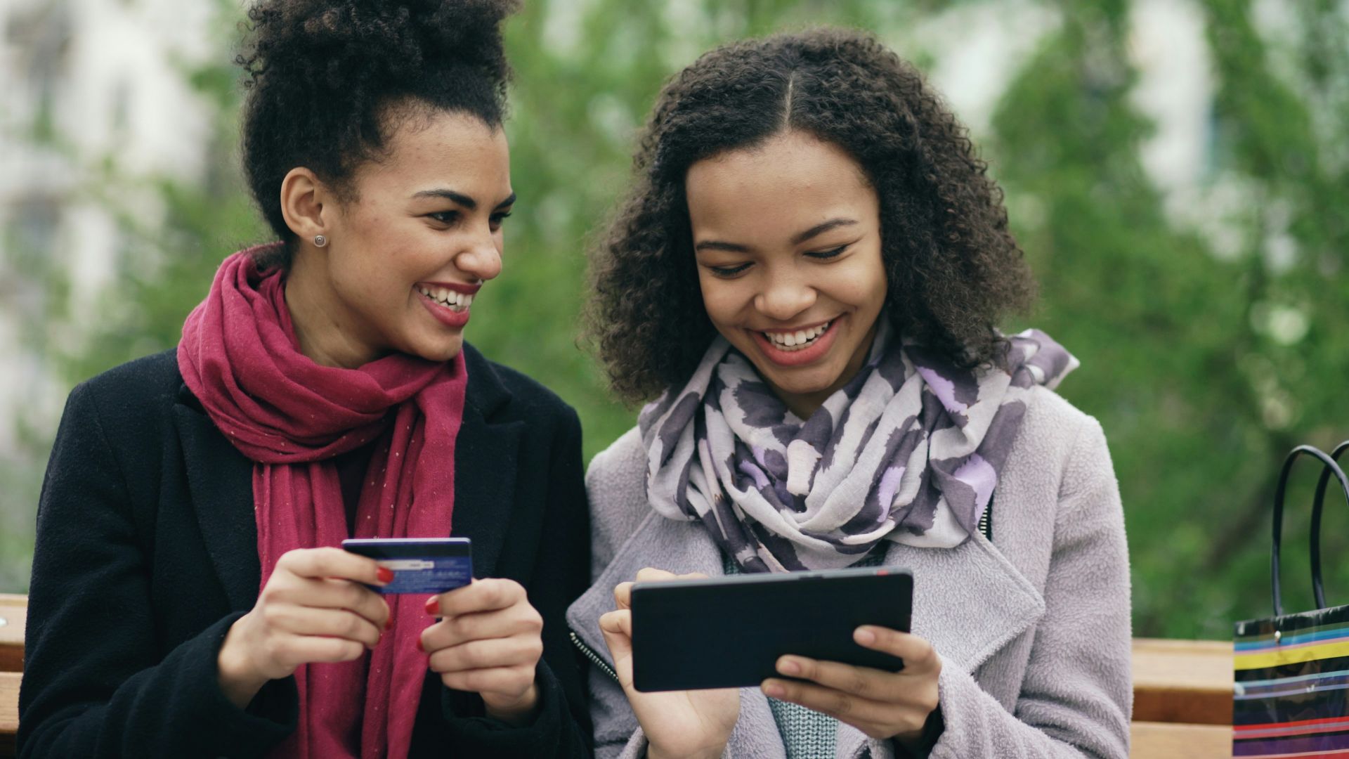 Two smiling women looking at a tablet with credit card.