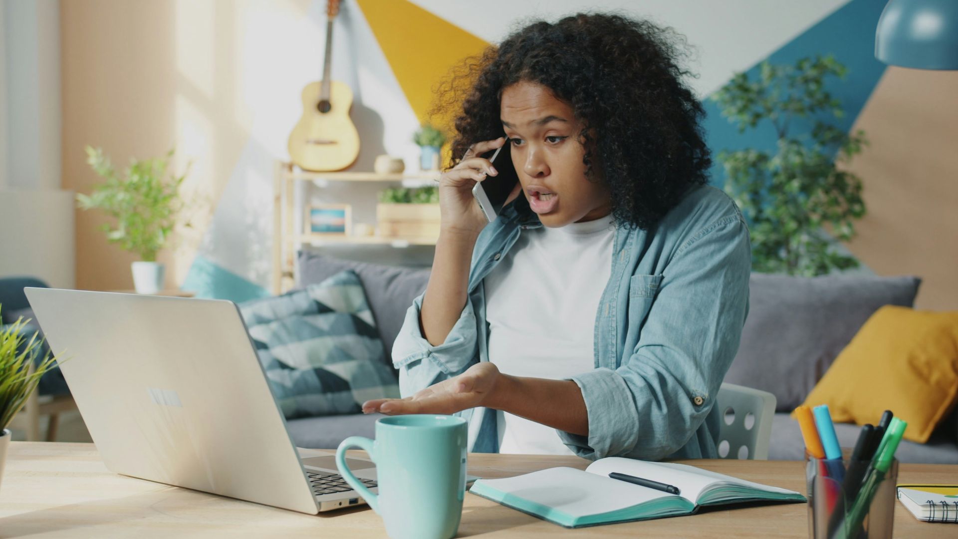 Young woman talking on phone at laptop desk.