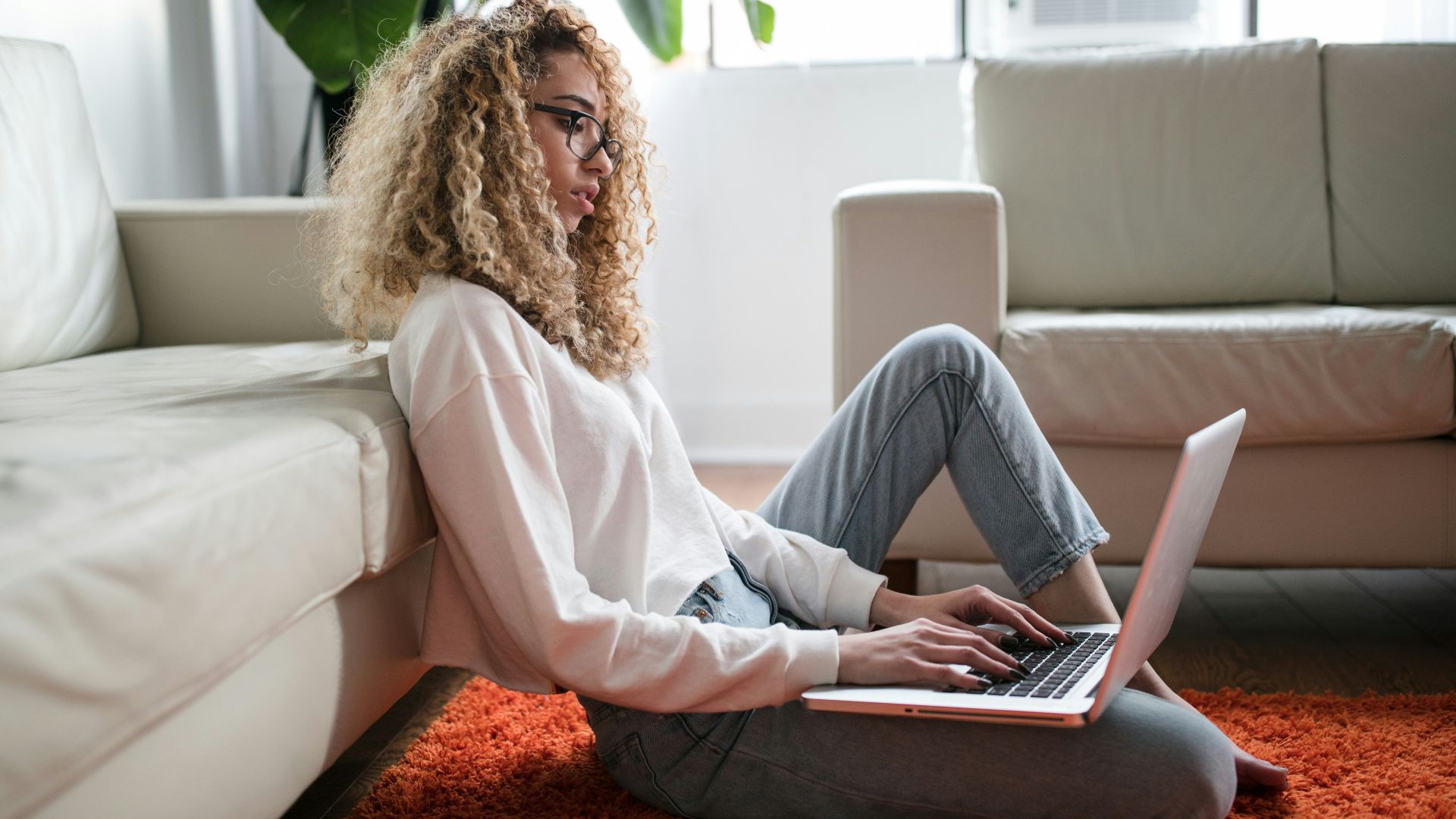 woman sitting on floor and leaning on couch using laptop