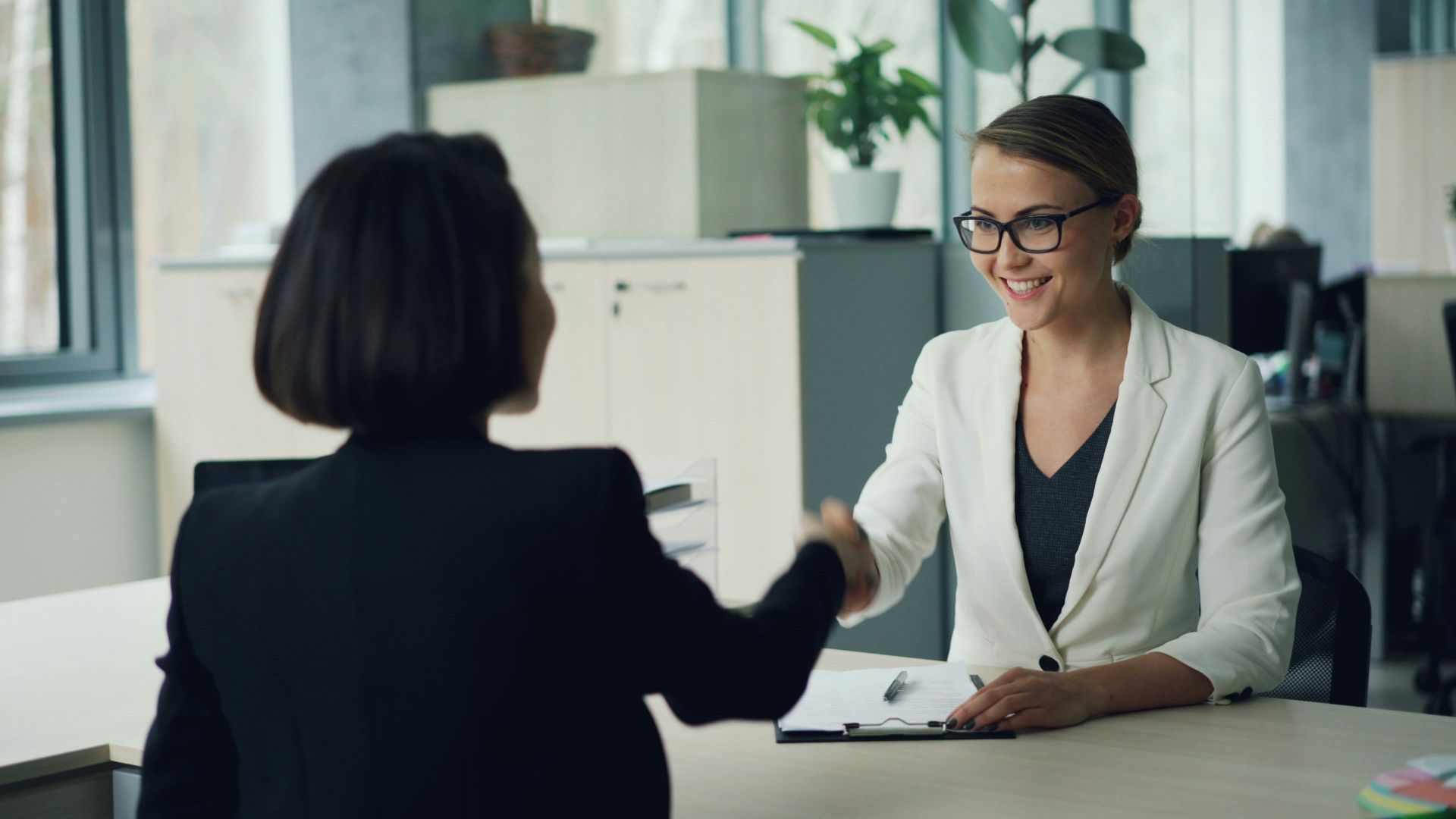 Two women shaking hands across a desk