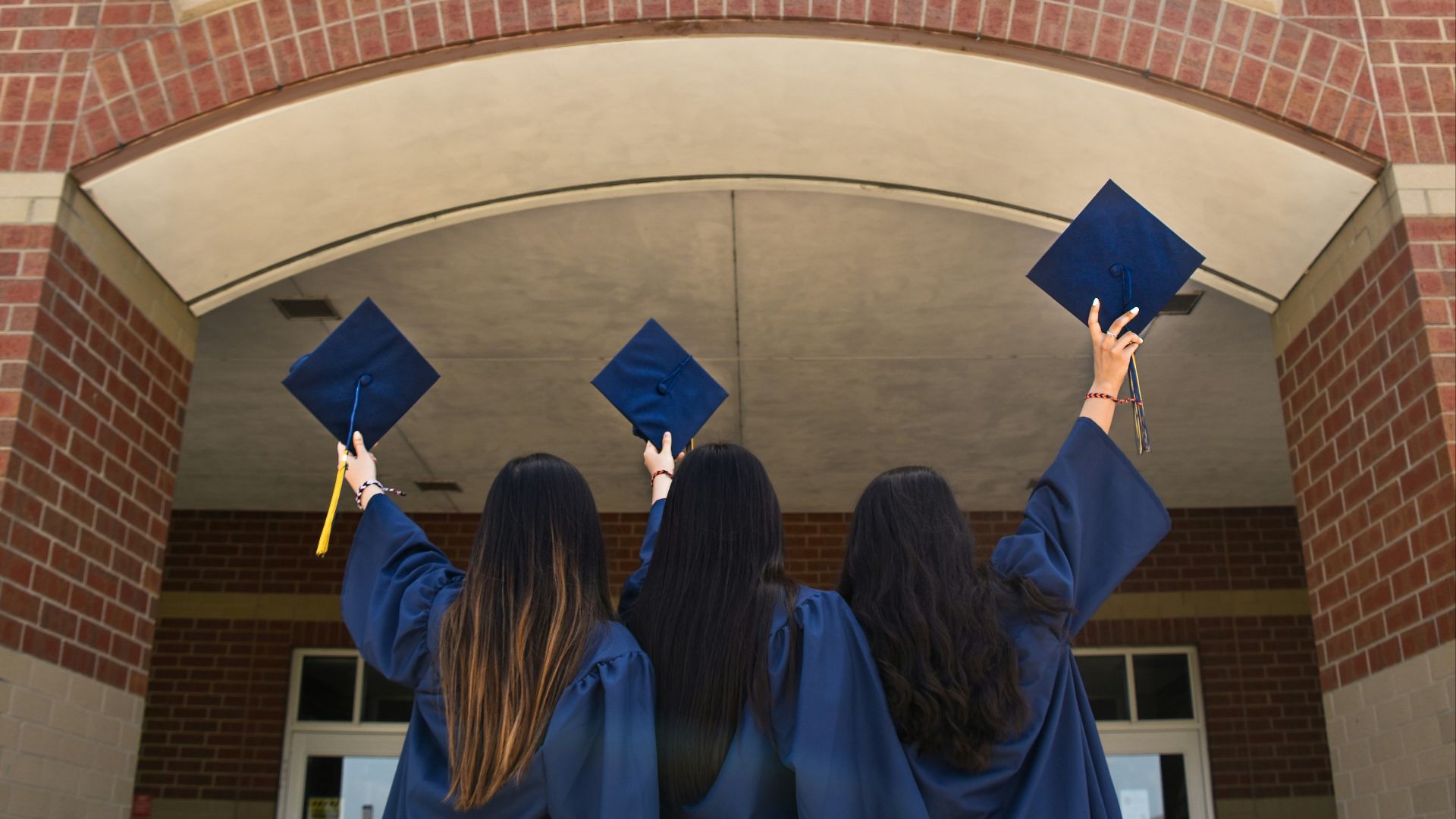 three girls in graduation gowns hold their caps in the air