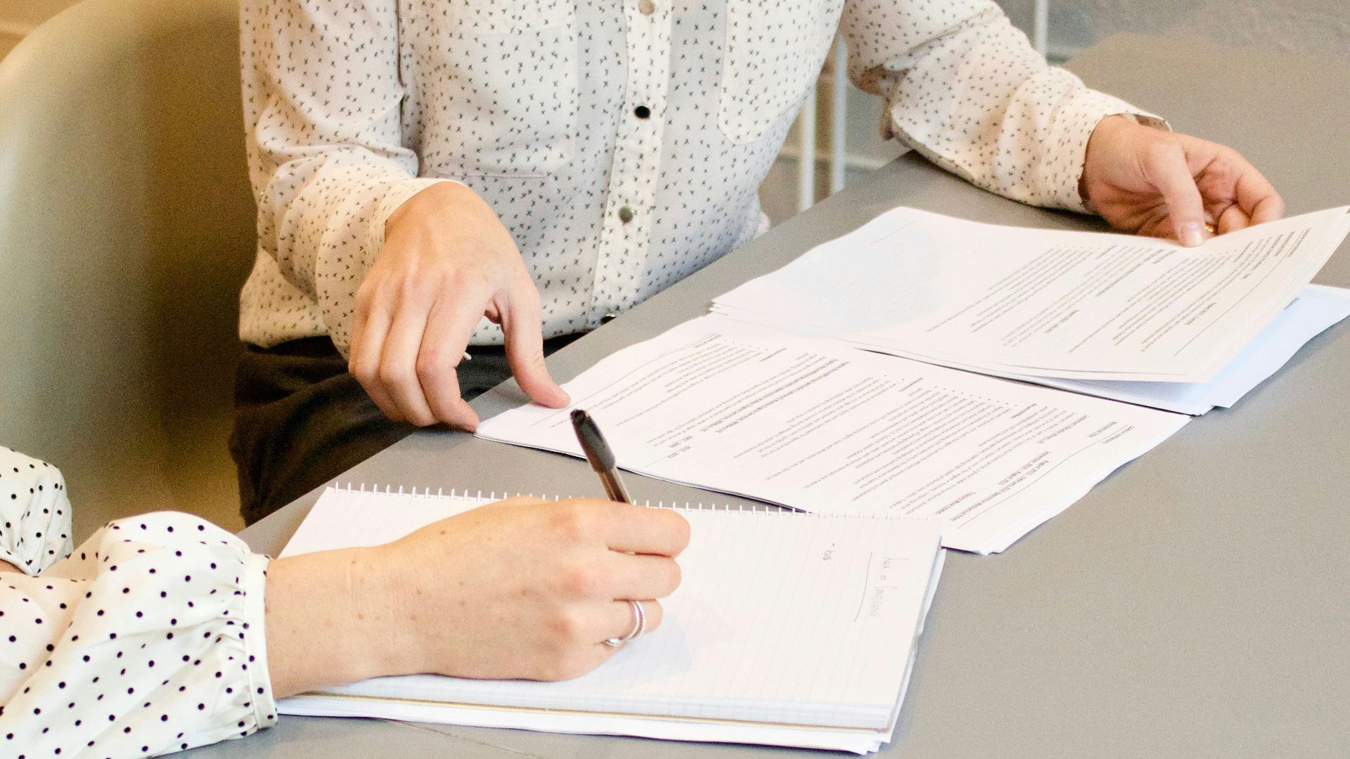 woman signing on white printer paper beside woman about to touch the documents