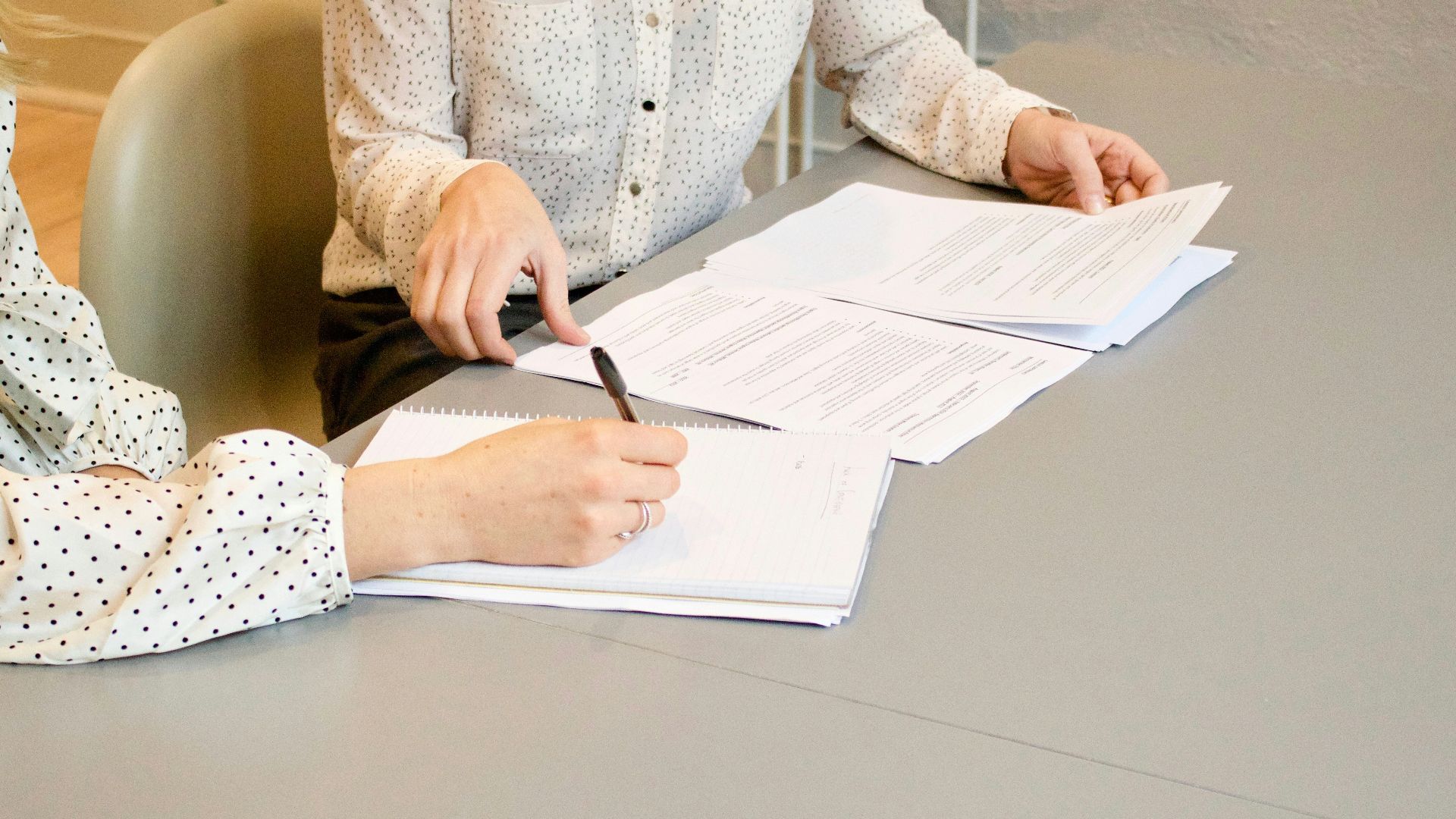 woman signing on white printer paper beside woman about to touch the documents