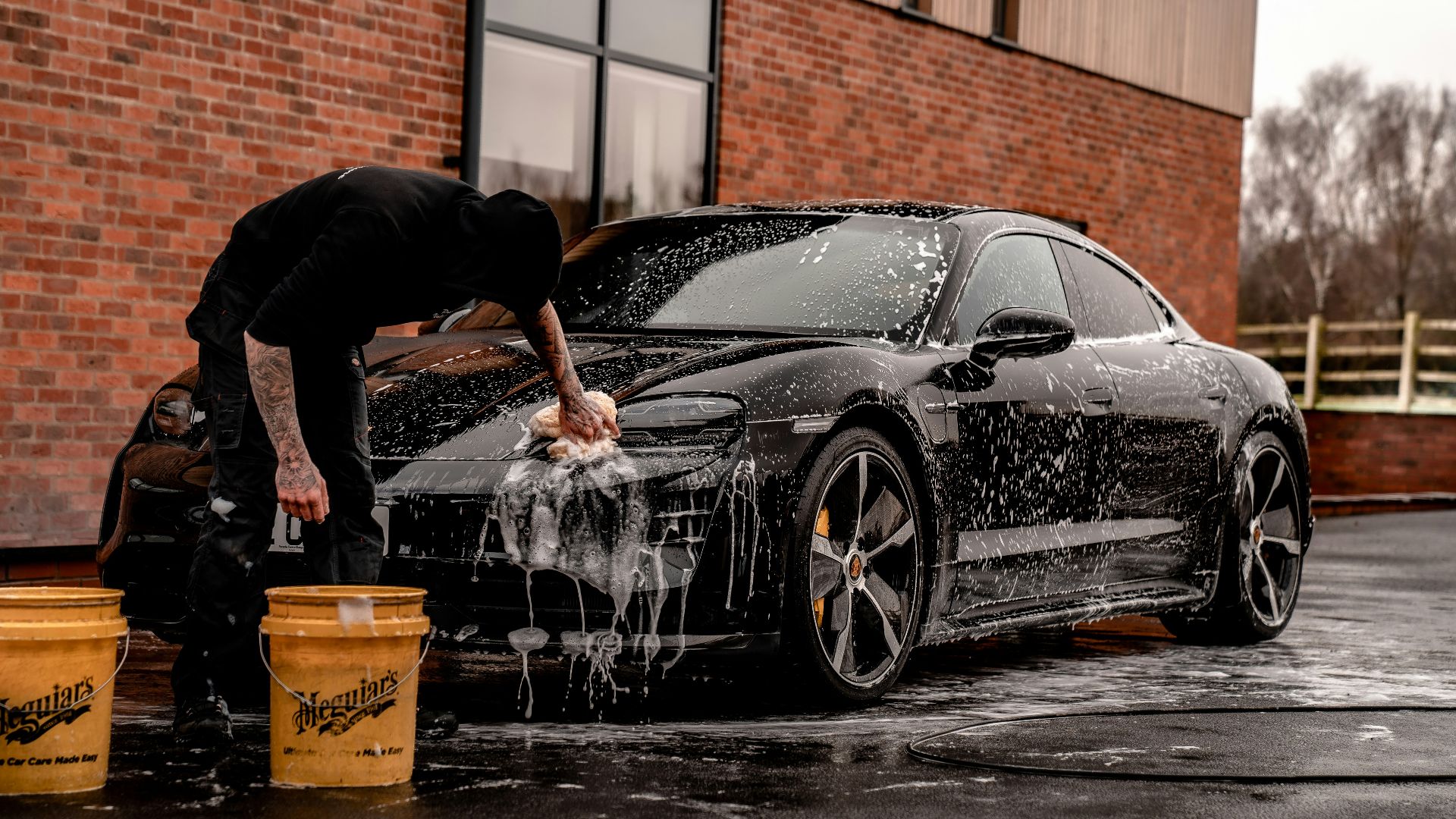 man in black t-shirt and black pants doing water splash on black coupe during daytime