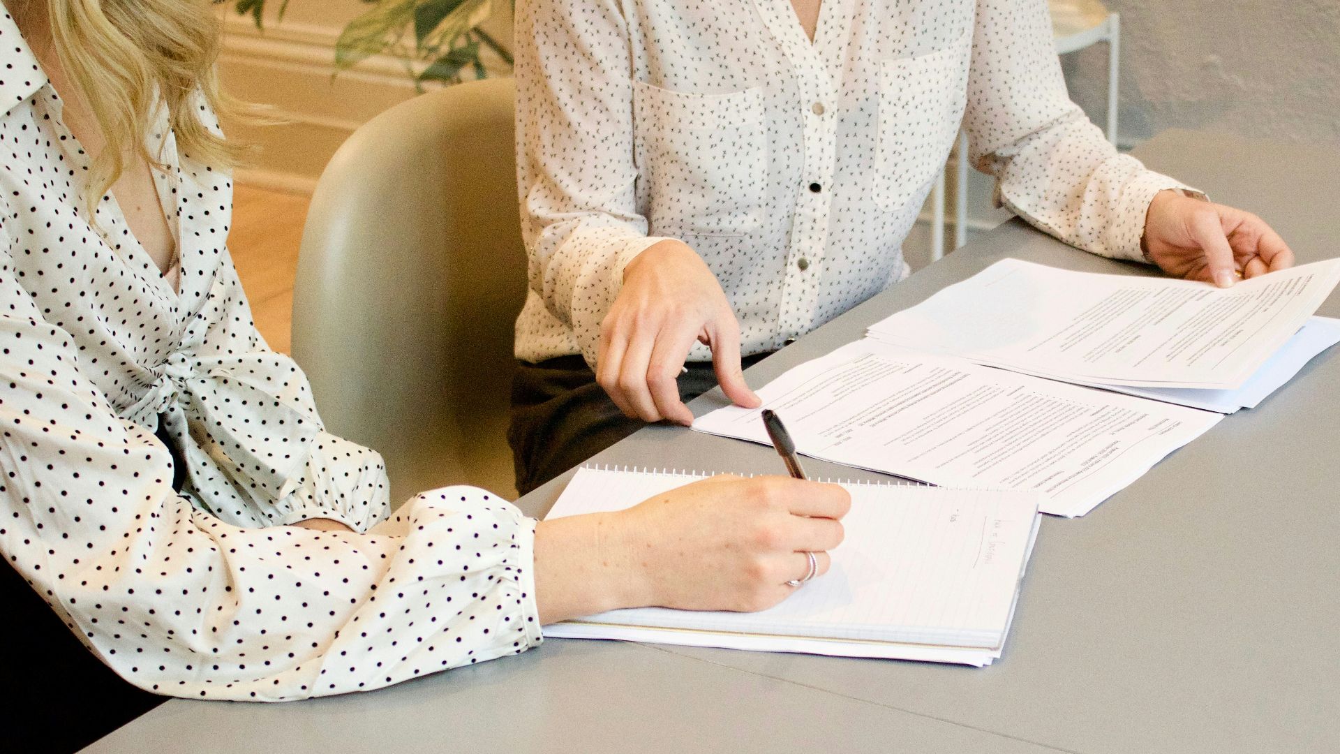 woman signing on white printer paper beside woman about to touch the documents