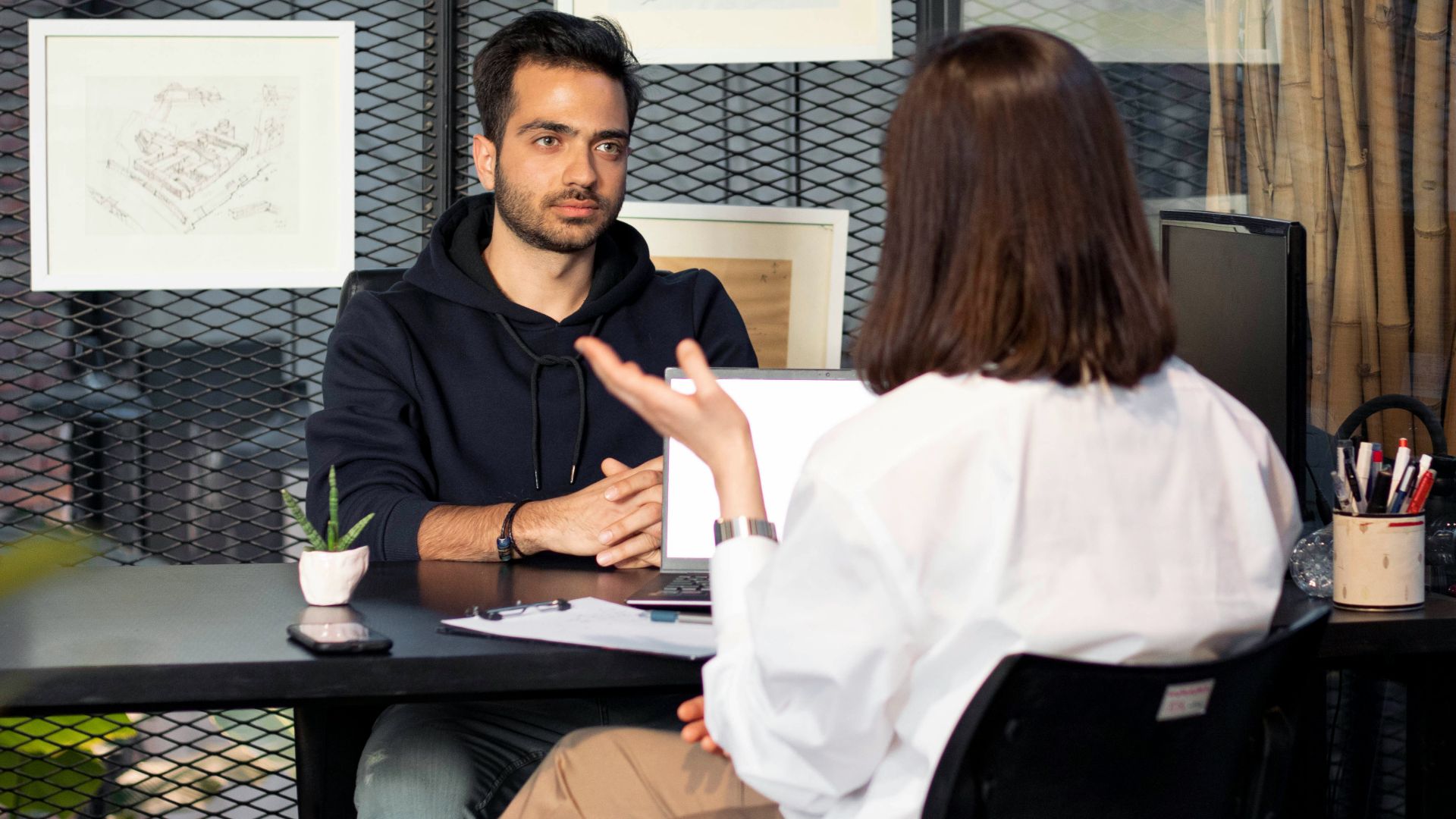 a man sitting at a desk talking to a woman