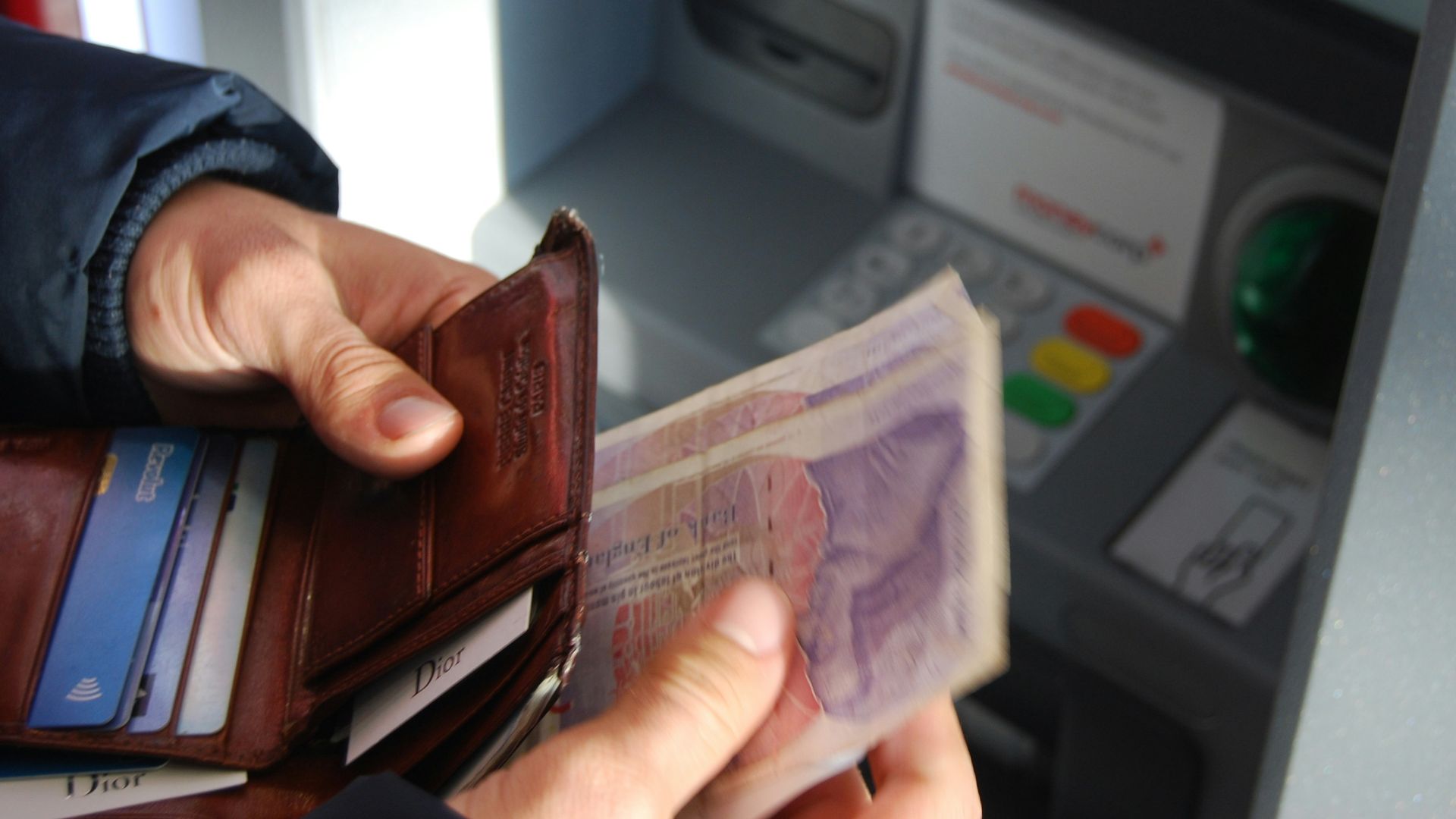person holding brown leather wallet and banknotes