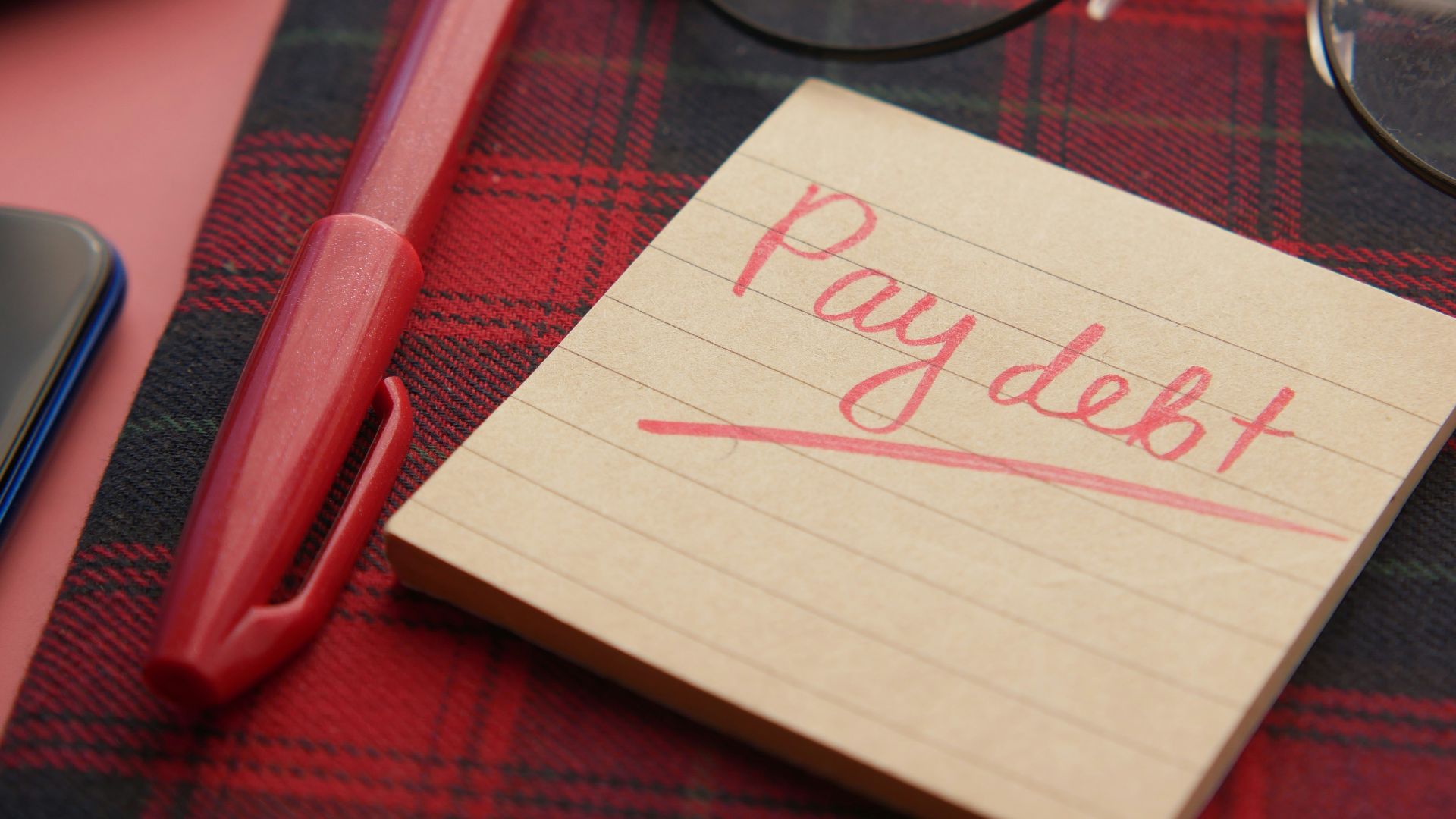 a note that says pay debt next to a pen and glasses