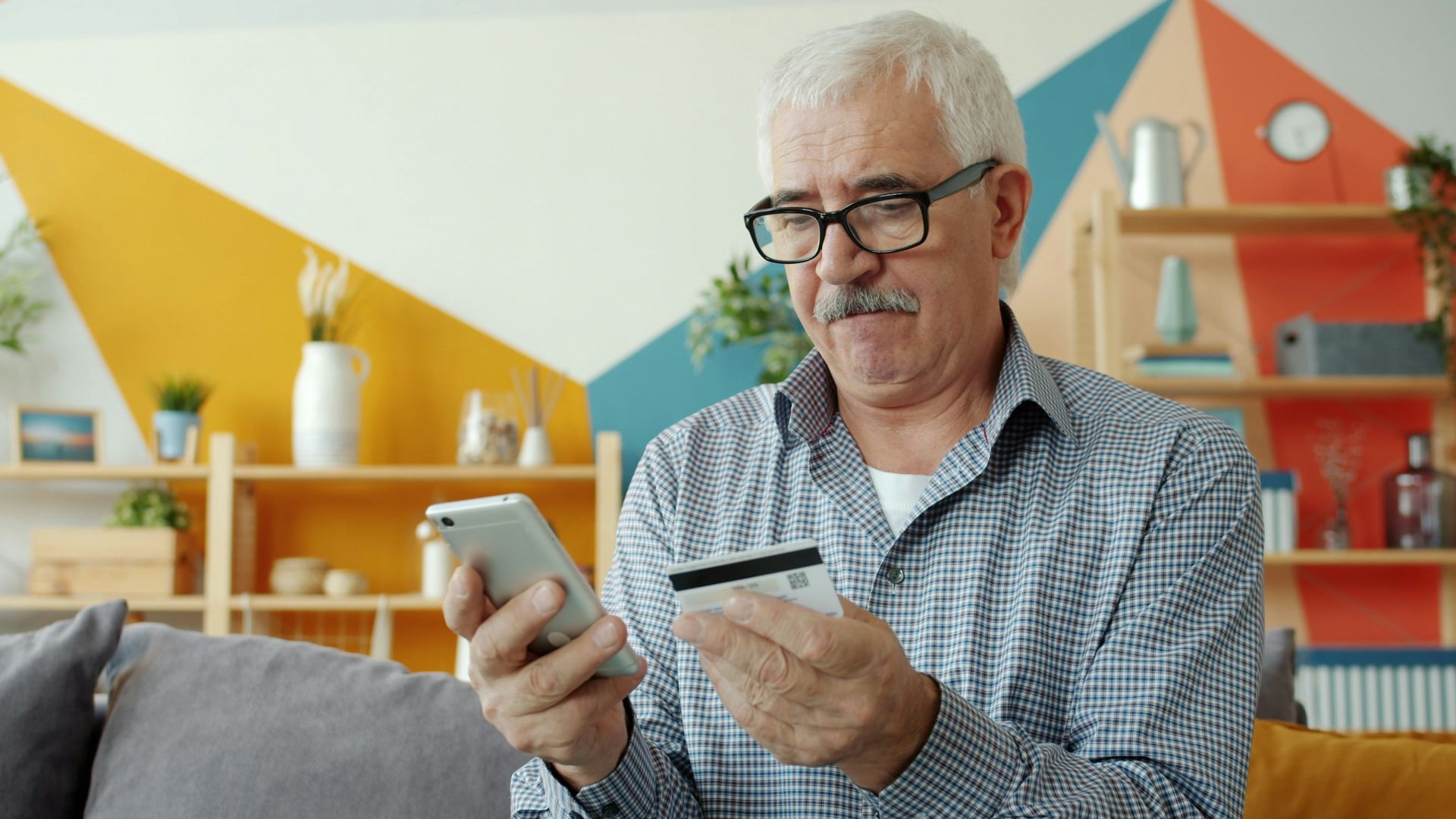 Elderly man using smartphone and credit card for online shopping.