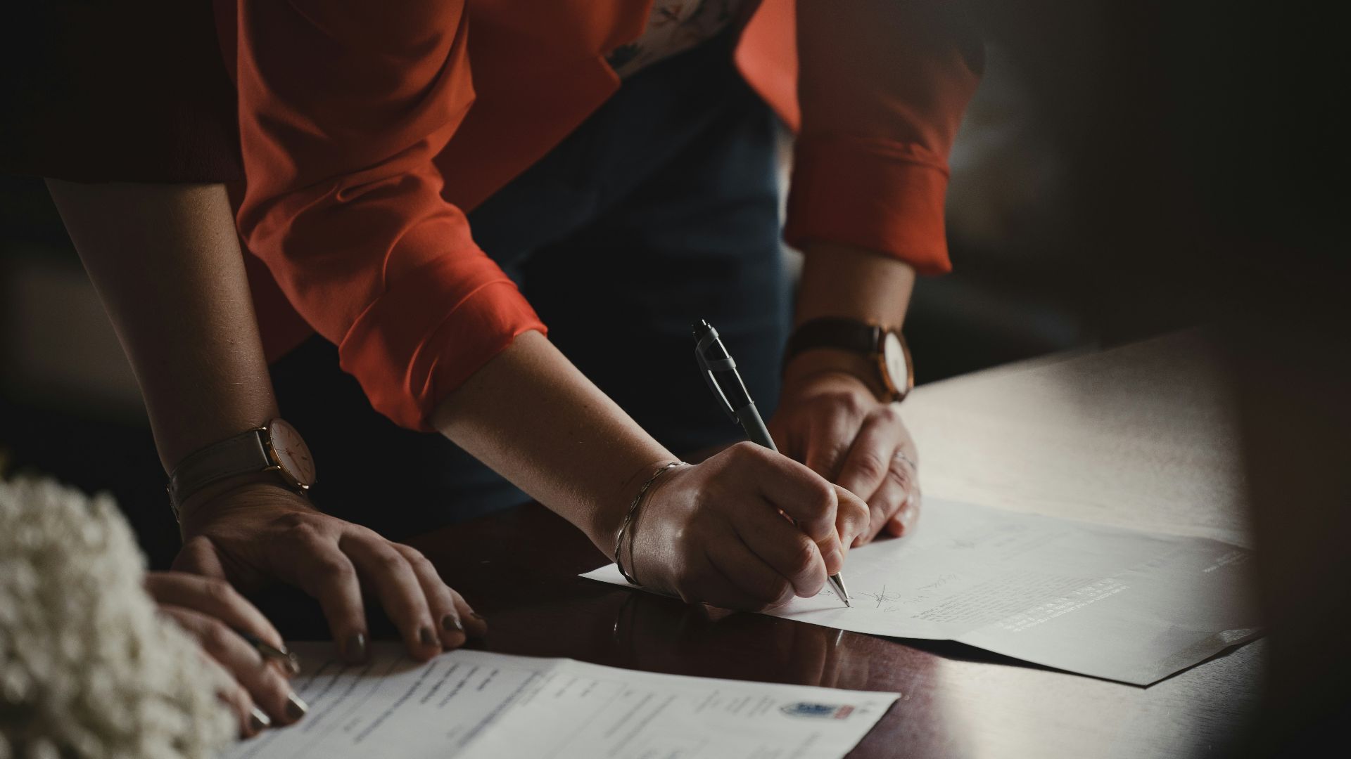 person in orange long sleeve shirt writing on white paper